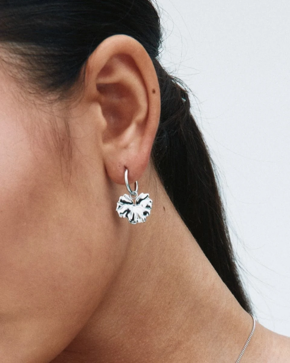 Hoops i polerat rostfritt stål med avtagbar charm som liknar ett stiliserat blomblad från Edblads Gerana-serie.