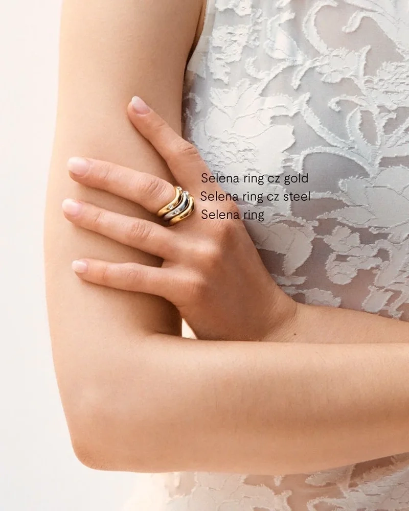 Två Selena ringar i stål och guld med vågformade skenor; en med cubic zirconia-stenar och en slät