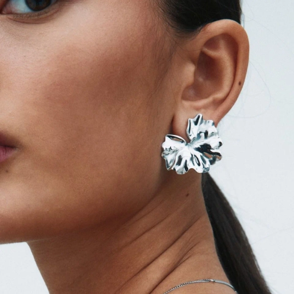 blanka örhängen i rostfritt stål med svepande blombladsform som elegant breder ut sig över örat.