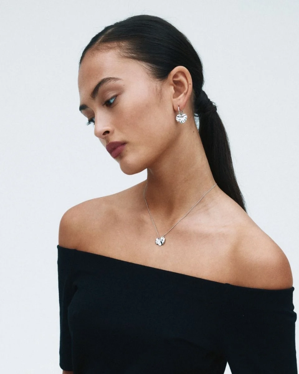 Hoops i polerat rostfritt stål med avtagbar charm som liknar ett stiliserat blomblad från Edblads Gerana-serie.