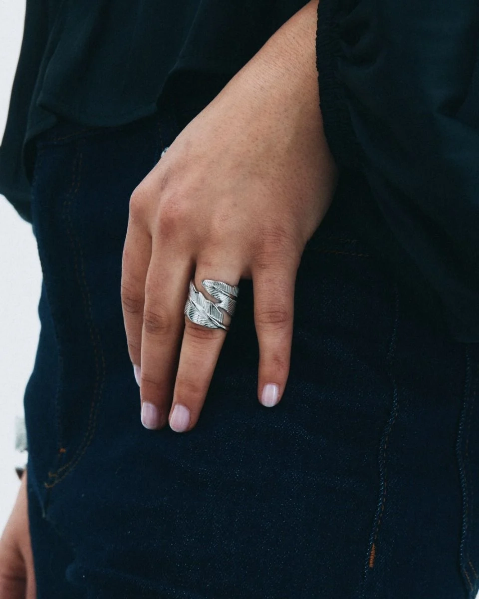 Stor silverring i polerat stål med två fjäderformade detaljer som slingrar sig runt fingret