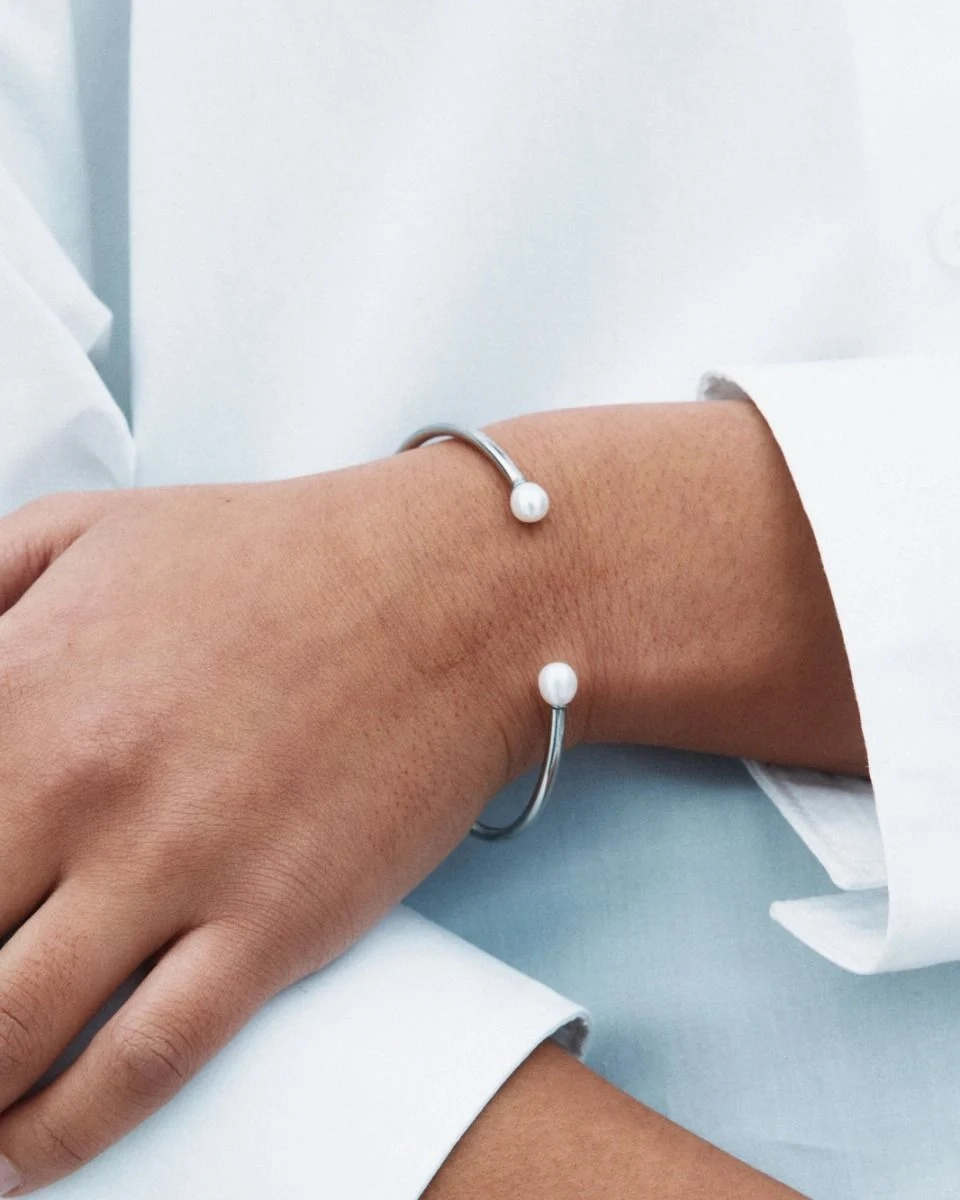 Armband i polerat rostfritt stål med öppen design och två pärlor i ändarna