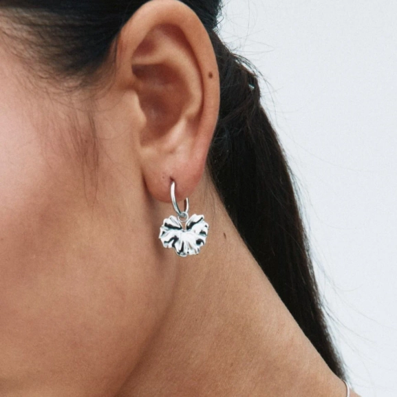 Hoops i polerat rostfritt stål med avtagbar charm som liknar ett stiliserat blomblad från Edblads Gerana-serie.