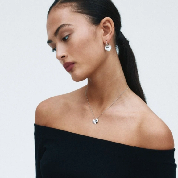 Hoops i polerat rostfritt stål med avtagbar charm som liknar ett stiliserat blomblad från Edblads Gerana-serie.