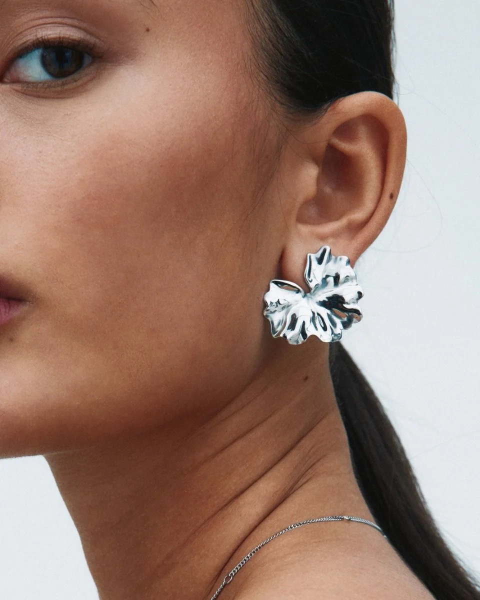 blanka örhängen i rostfritt stål med svepande blombladsform som elegant breder ut sig över örat.