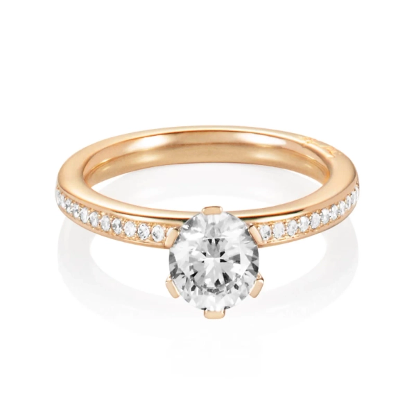 ring i 18K gult guld med en stor briljantslipad diamant och mindre pavédiamanter längs skenan.