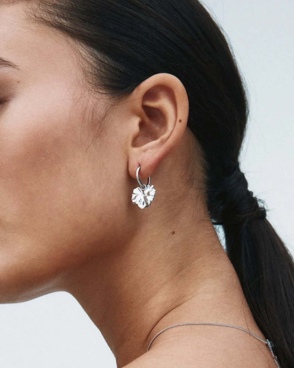 Hoops i polerat rostfritt stål med avtagbar charm som liknar ett stiliserat blomblad från Edblads Gerana-serie.