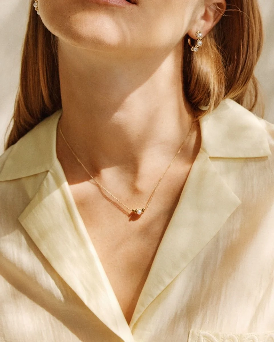 Elegant halsband i 14K guldpläterat stål med tvinnad design och skimrande pärlemorpärla på stilren pansarkedja.